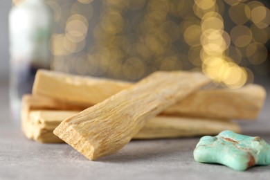 Photo of Palo santo sticks and gemstone on grey table against blurred lights, closeup