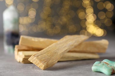 Photo of Palo santo sticks and gemstone on grey table against blurred lights, closeup