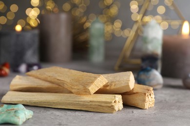 Photo of Palo santo sticks and gemstones on grey table against blurred lights, closeup