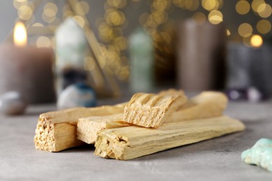 Photo of Palo santo sticks and gemstones on grey table against blurred lights, closeup