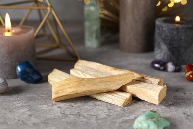 Photo of Palo santo sticks, gemstones and burning candles on grey table, closeup