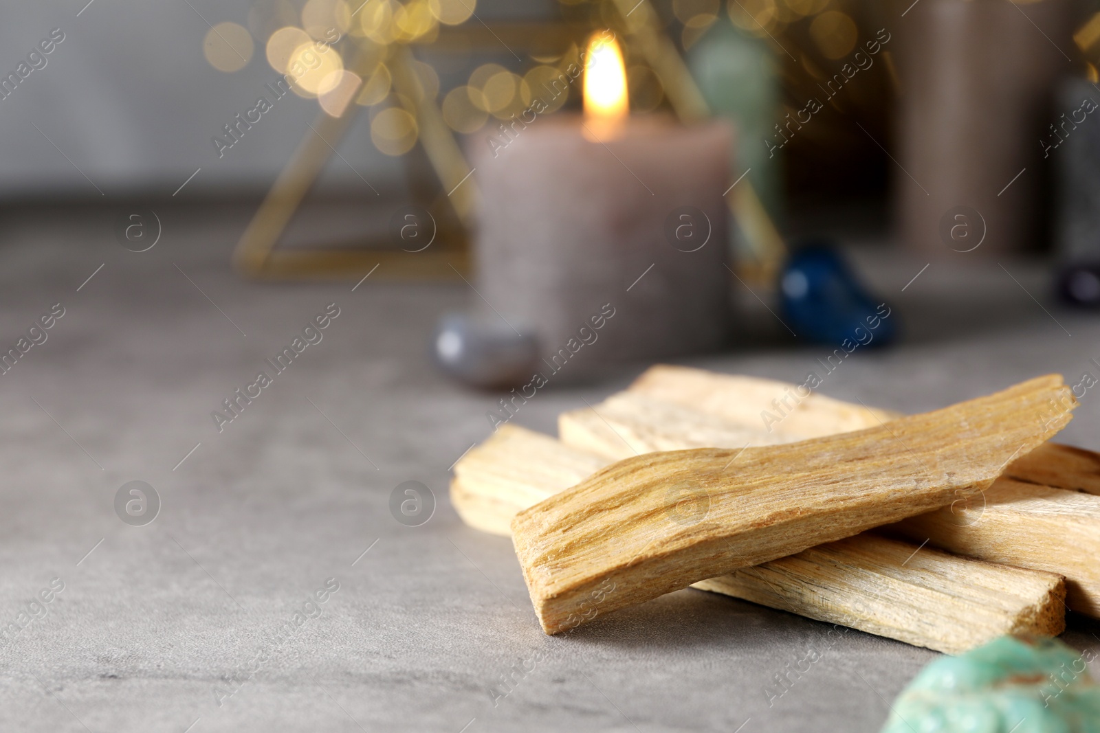 Photo of Palo santo sticks, gemstones and burning candles on grey table, closeup. Space for text