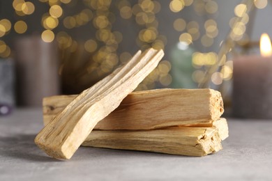 Photo of Palo santo sticks on grey table against blurred lights, closeup