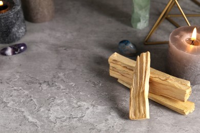 Photo of Palo santo sticks, gemstones and burning candles on grey table. Space for text