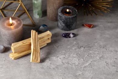 Photo of Palo santo sticks, gemstones and burning candles on grey table. Space for text