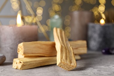 Photo of Palo santo sticks and burning candles on grey table, closeup