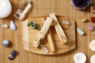 Photo of Palo santo sticks and gemstones on wicker table, flat lay