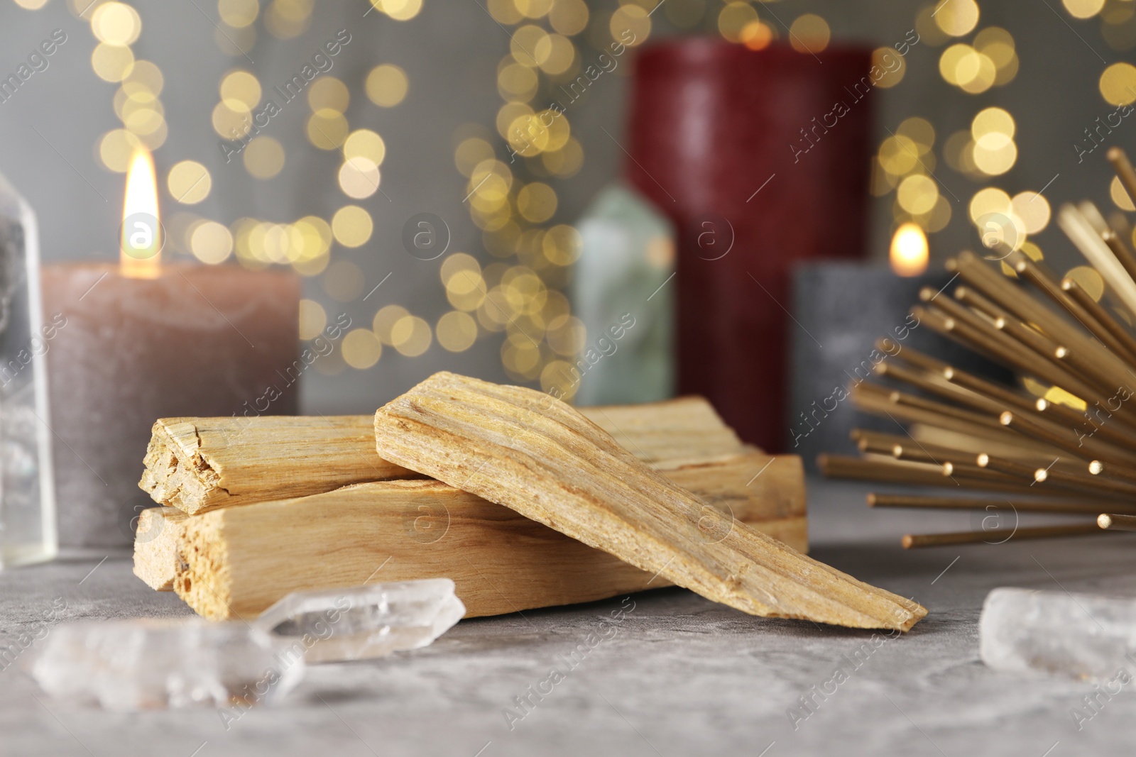 Photo of Palo santo sticks and gemstones on grey table against blurred lights