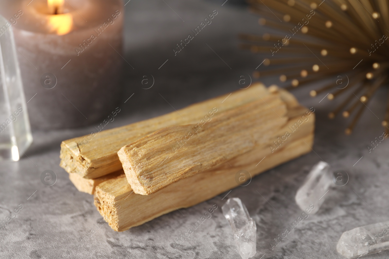 Photo of Palo santo sticks, gemstones and burning candle on grey table, closeup