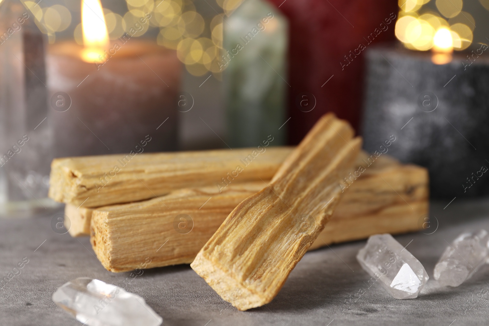 Photo of Palo santo sticks, gemstones and burning candles on grey table, closeup