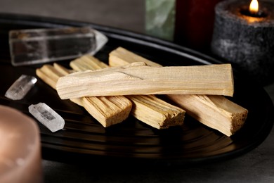 Photo of Palo santo sticks, gemstones and burning candles on grey table, closeup