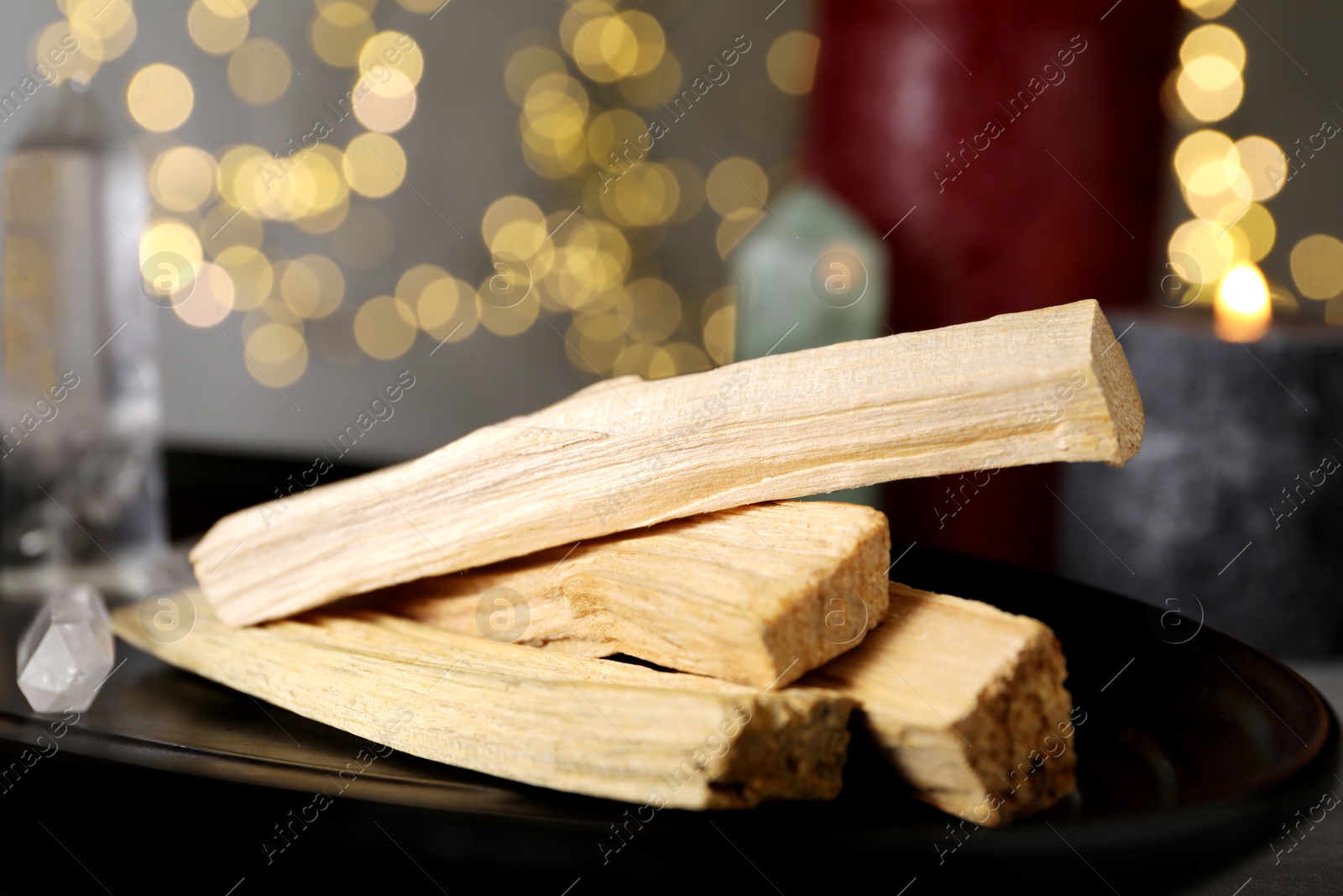 Photo of Palo santo sticks and gemstone on table against blurred lights, closeup