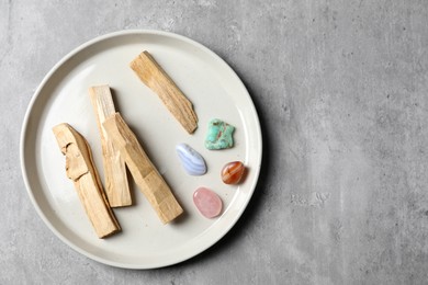 Photo of Palo santo sticks and gemstones on grey table, top view. Space for text