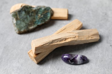 Photo of Palo santo sticks and gemstones on grey table, closeup