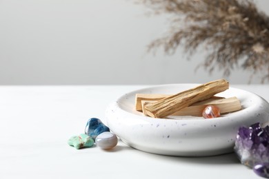 Photo of Palo santo sticks and gemstones on white table. Space for text