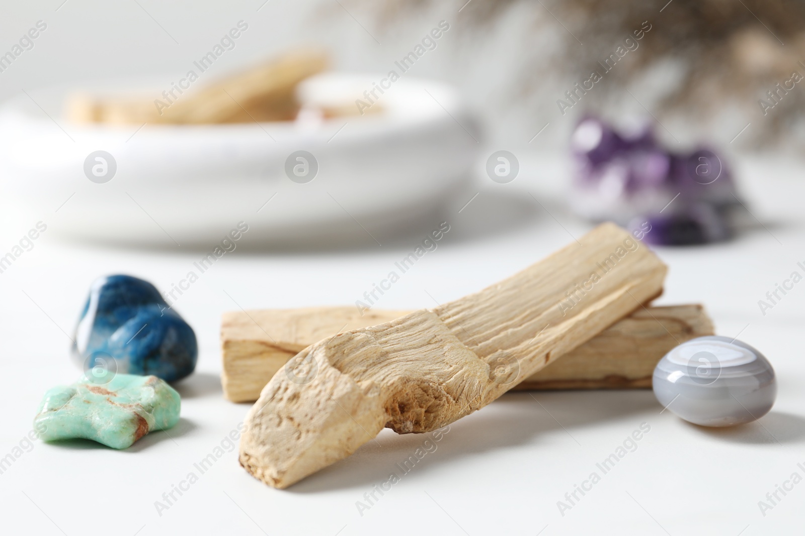 Photo of Palo santo sticks and gemstones on white table, closeup