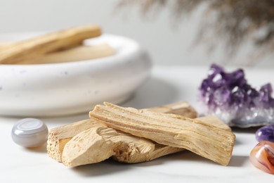 Photo of Palo santo sticks and gemstones on white table, closeup