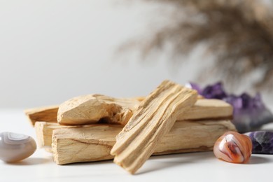 Photo of Palo santo sticks and gemstones on white table, closeup. Space for text