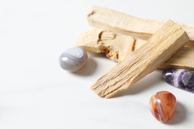 Photo of Palo santo sticks and gemstones on white table, closeup. Space for text