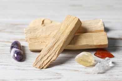 Photo of Palo santo sticks and gemstones on white wooden table, closeup