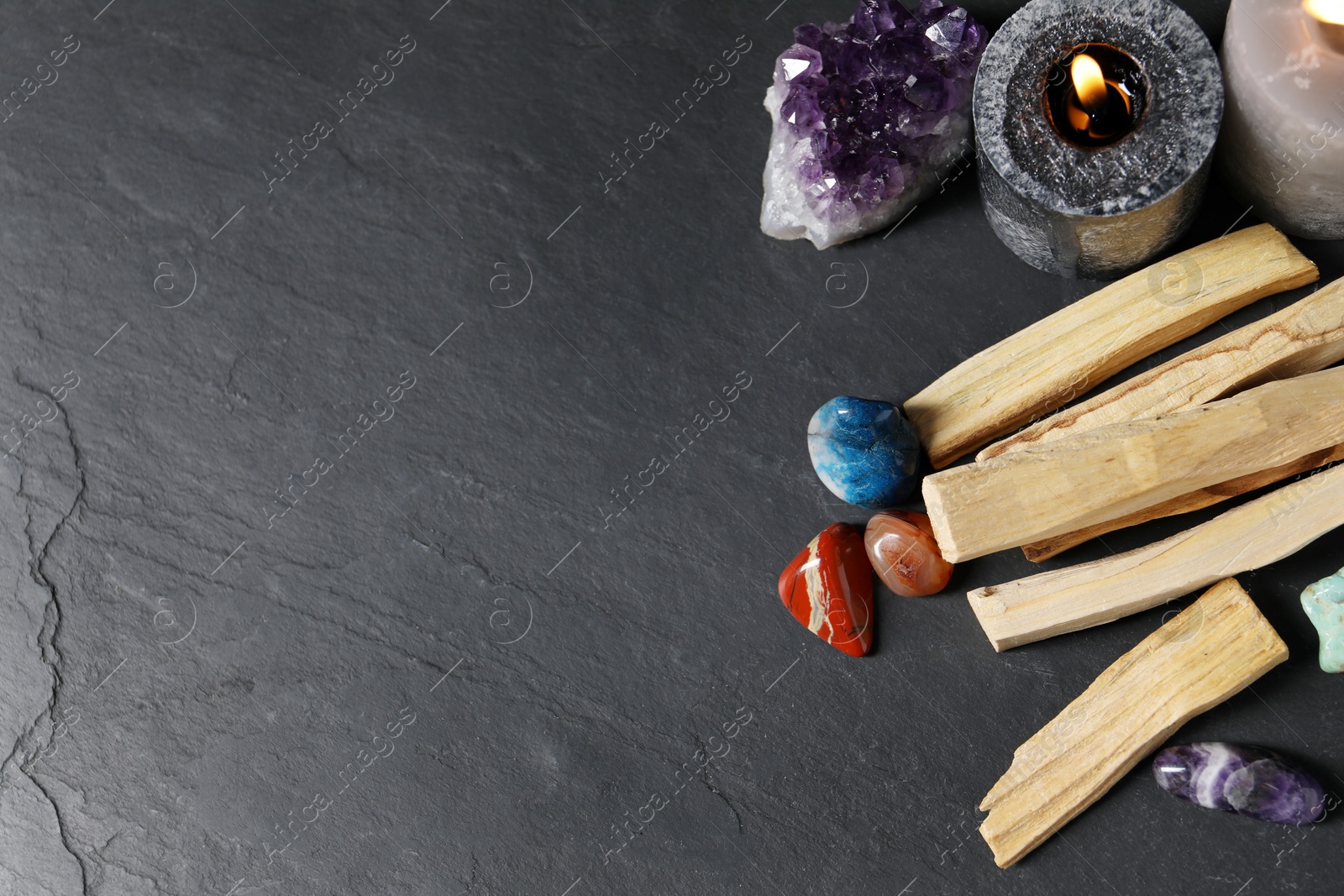 Photo of Palo santo sticks, gemstones and burning candles on black table, flat lay. Space for text