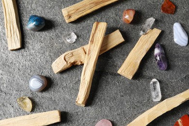 Photo of Palo santo sticks and gemstones on grey table, flat lay