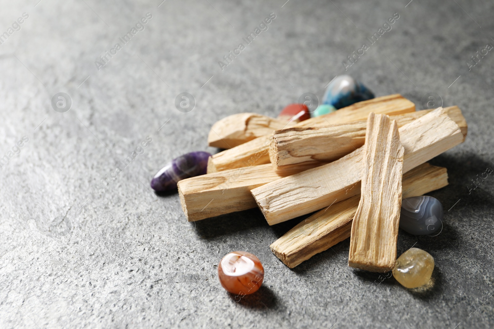 Photo of Palo santo sticks and gemstones on grey table. Space for text