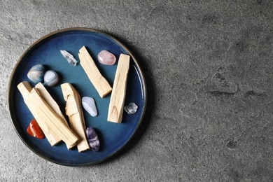 Photo of Palo santo sticks and gemstones on grey table, top view. Space for text