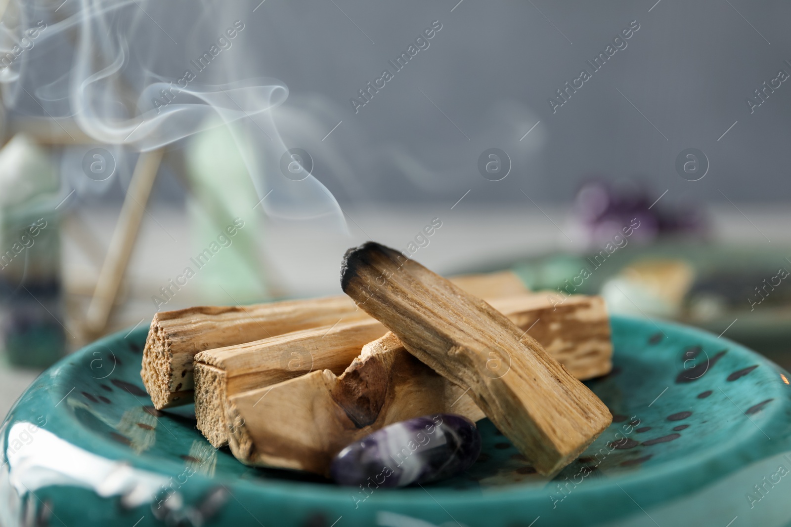 Photo of Smoldering palo santo stick and gemstone on table, closeup