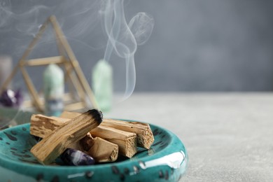 Photo of Smoldering palo santo stick and gemstone on light grey table, closeup. Space for text