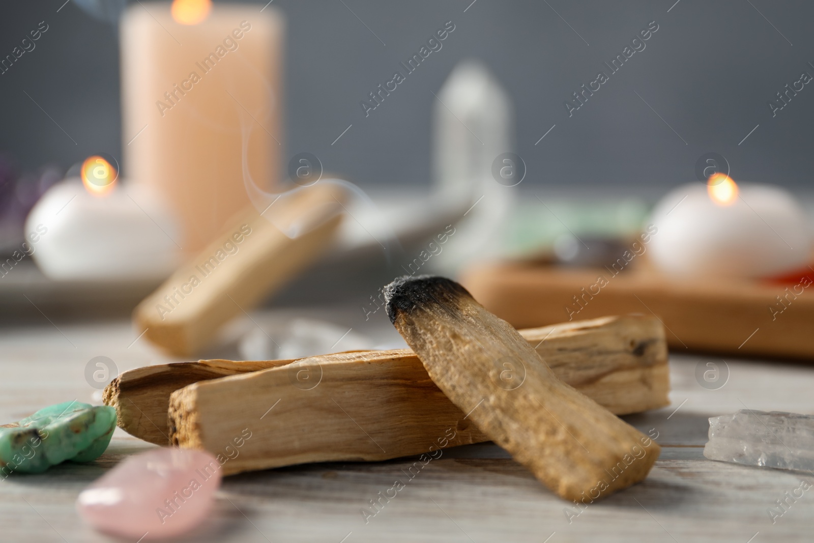 Photo of Smoldering palo santo stick and gemstones on wooden table, closeup