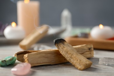 Photo of Smoldering palo santo stick and gemstones on wooden table, closeup