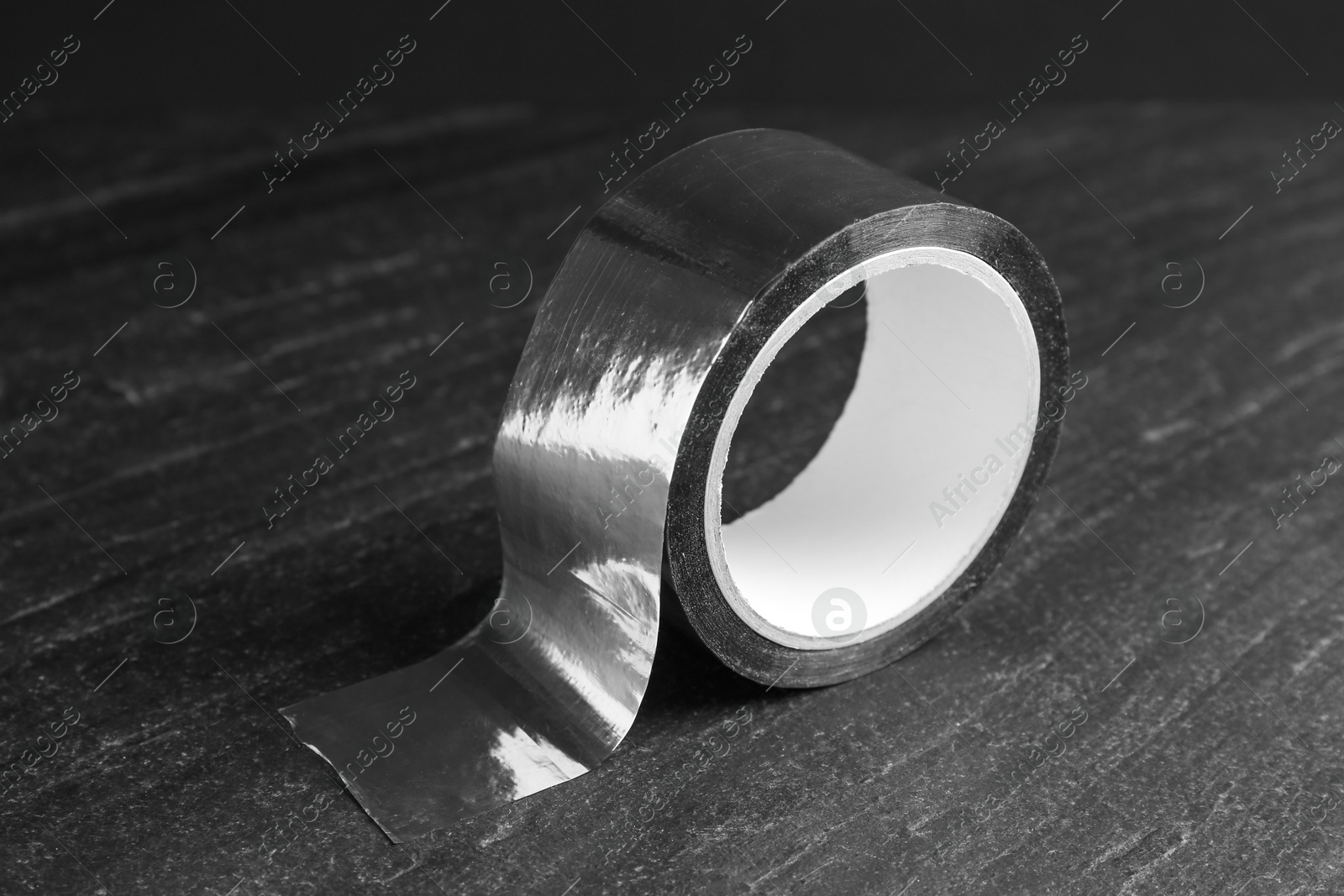 Photo of Roll of silver adhesive tape on black table, closeup