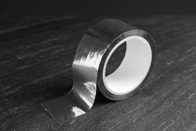 Photo of Roll of silver adhesive tape on black table, closeup