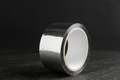 Roll of silver adhesive tape on black table, closeup