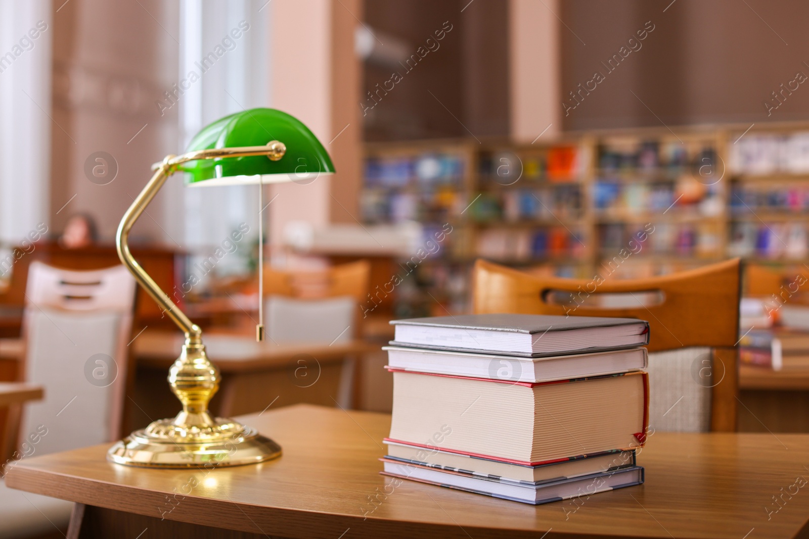 Photo of Stack of books and beautiful lamp on wooden desk in library