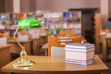 Photo of Stack of books and beautiful lamp on wooden desk in library