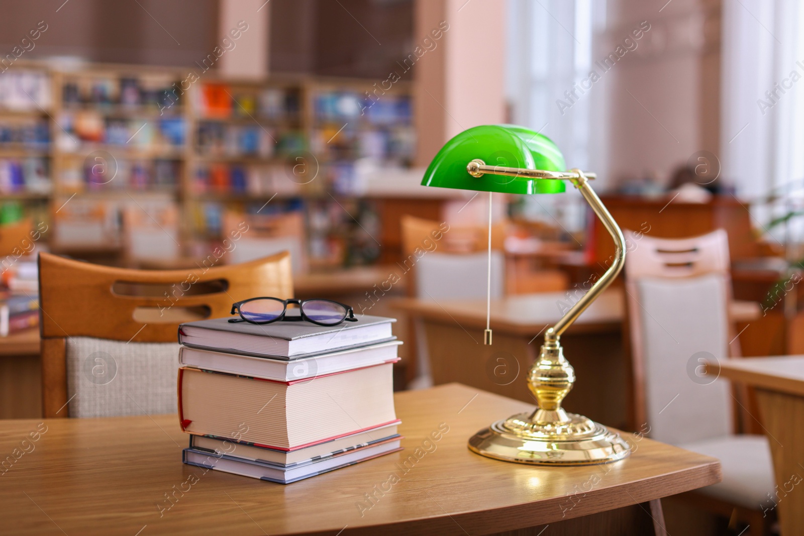 Photo of Stack of books, glasses and beautiful lamp on wooden desk in library