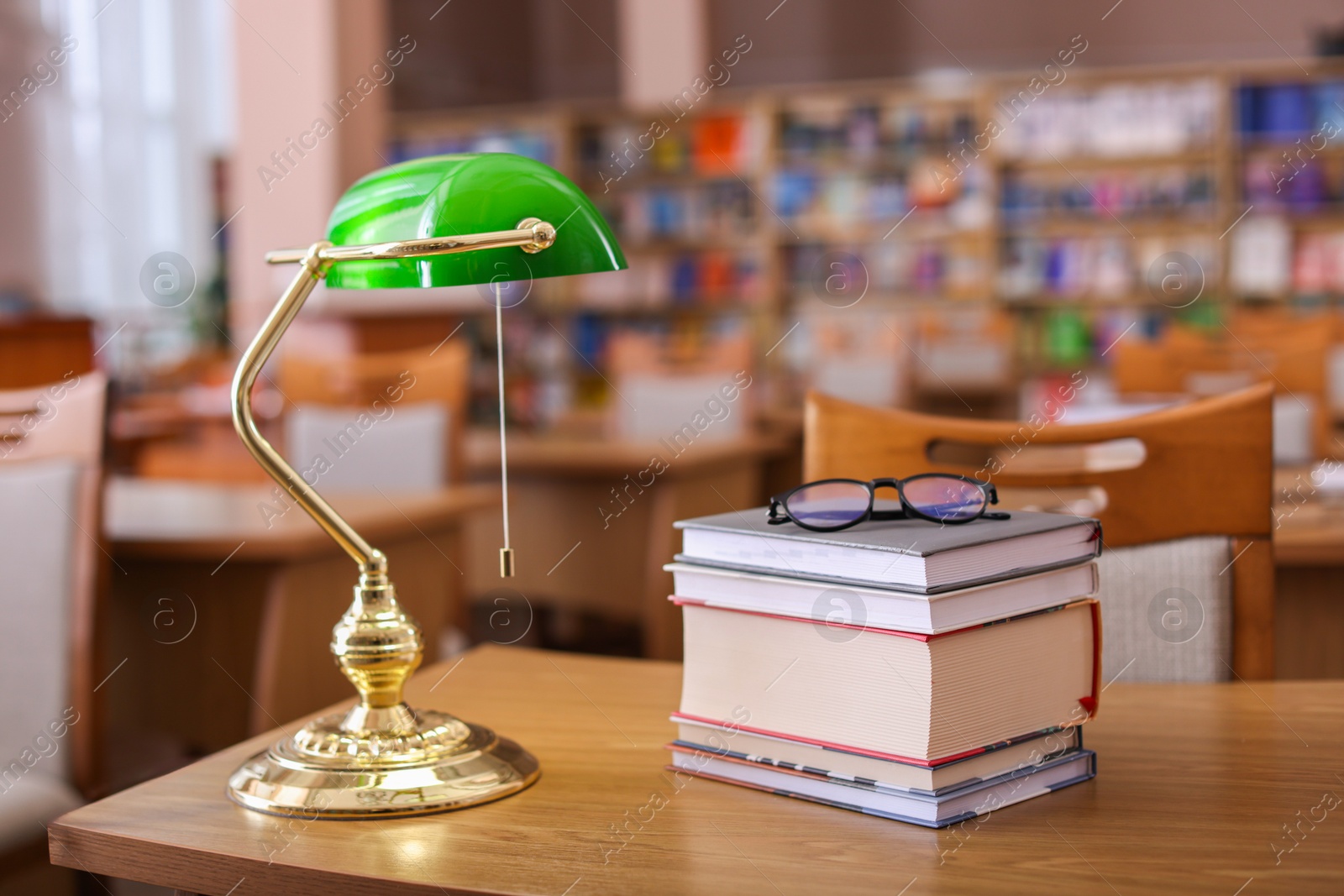 Photo of Stack of books, glasses and beautiful lamp on wooden desk in library