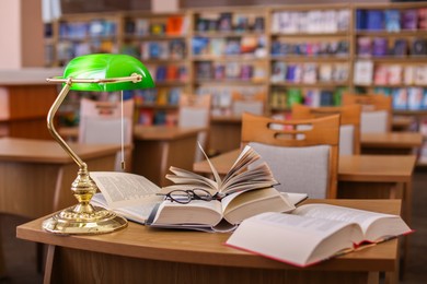 Photo of Different books, glasses and beautiful lamp on wooden desk in library