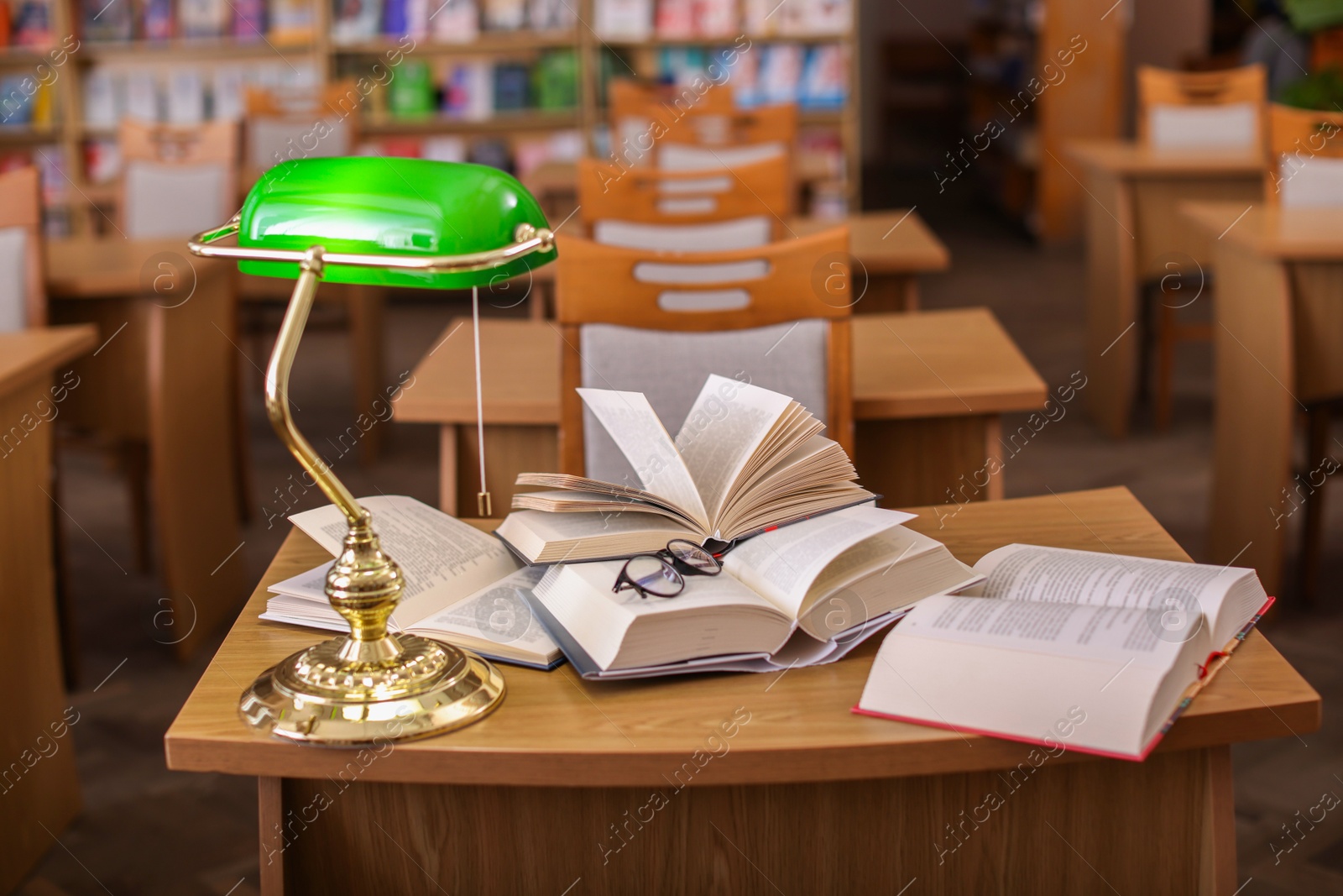 Photo of Different books, glasses and beautiful lamp on wooden desk in library