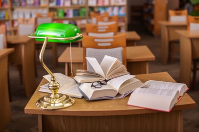 Photo of Different books, glasses and beautiful lamp on wooden desk in library