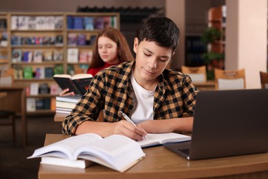 Photo of Boy taking notes at desk in public library