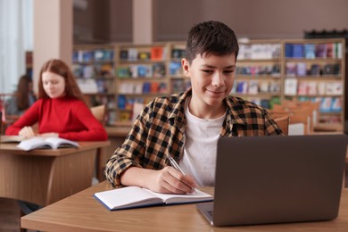 Photo of Boy taking notes at desk in public library