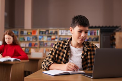 Photo of Boy taking notes at desk in public library