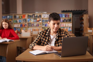 Photo of Boy taking notes at desk in public library