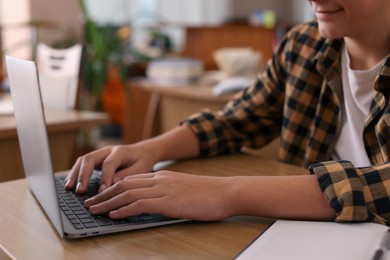 Photo of Boy using laptop at wooden desk in public library, closeup