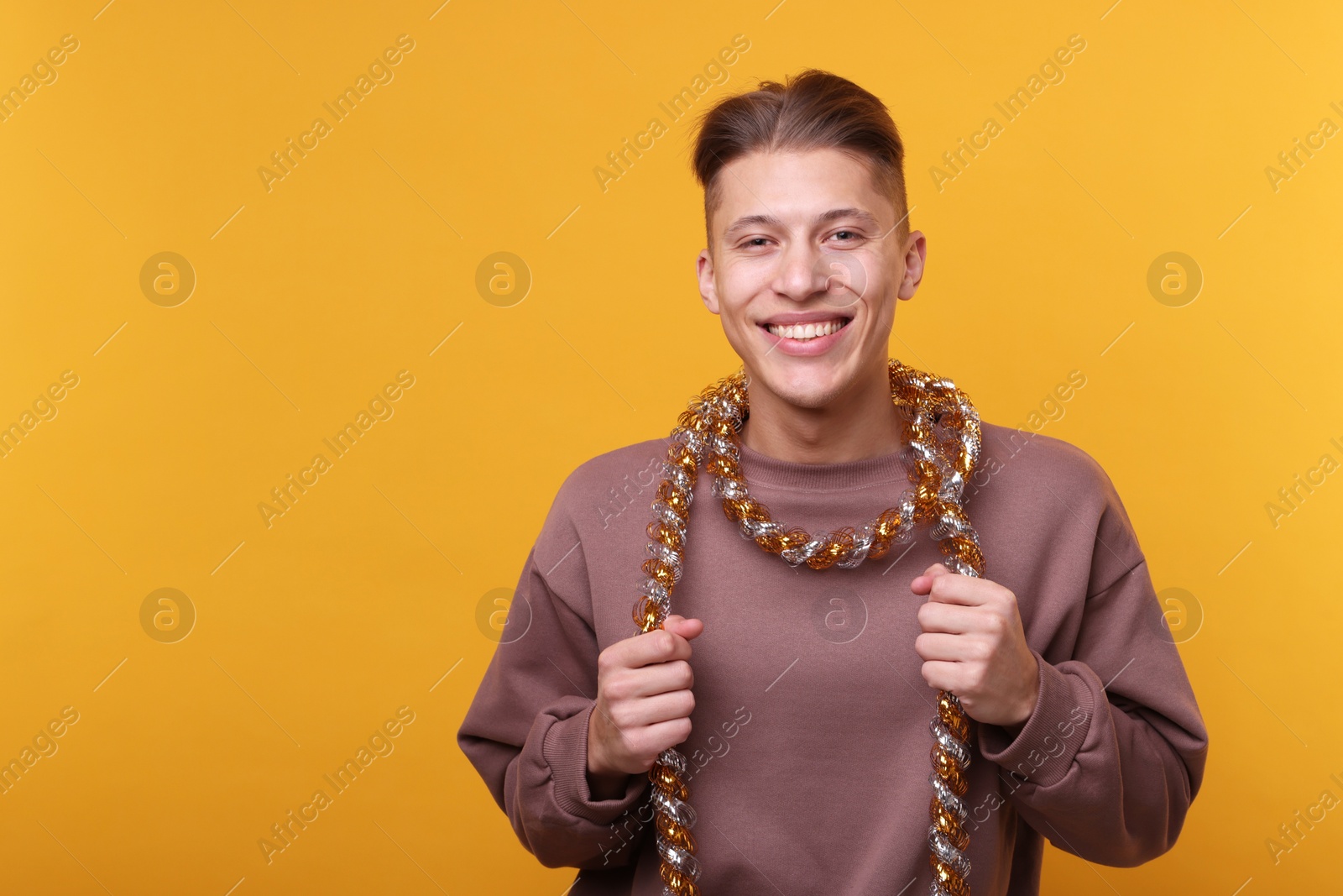 Photo of Happy young man with tinsel on orange background, space for text