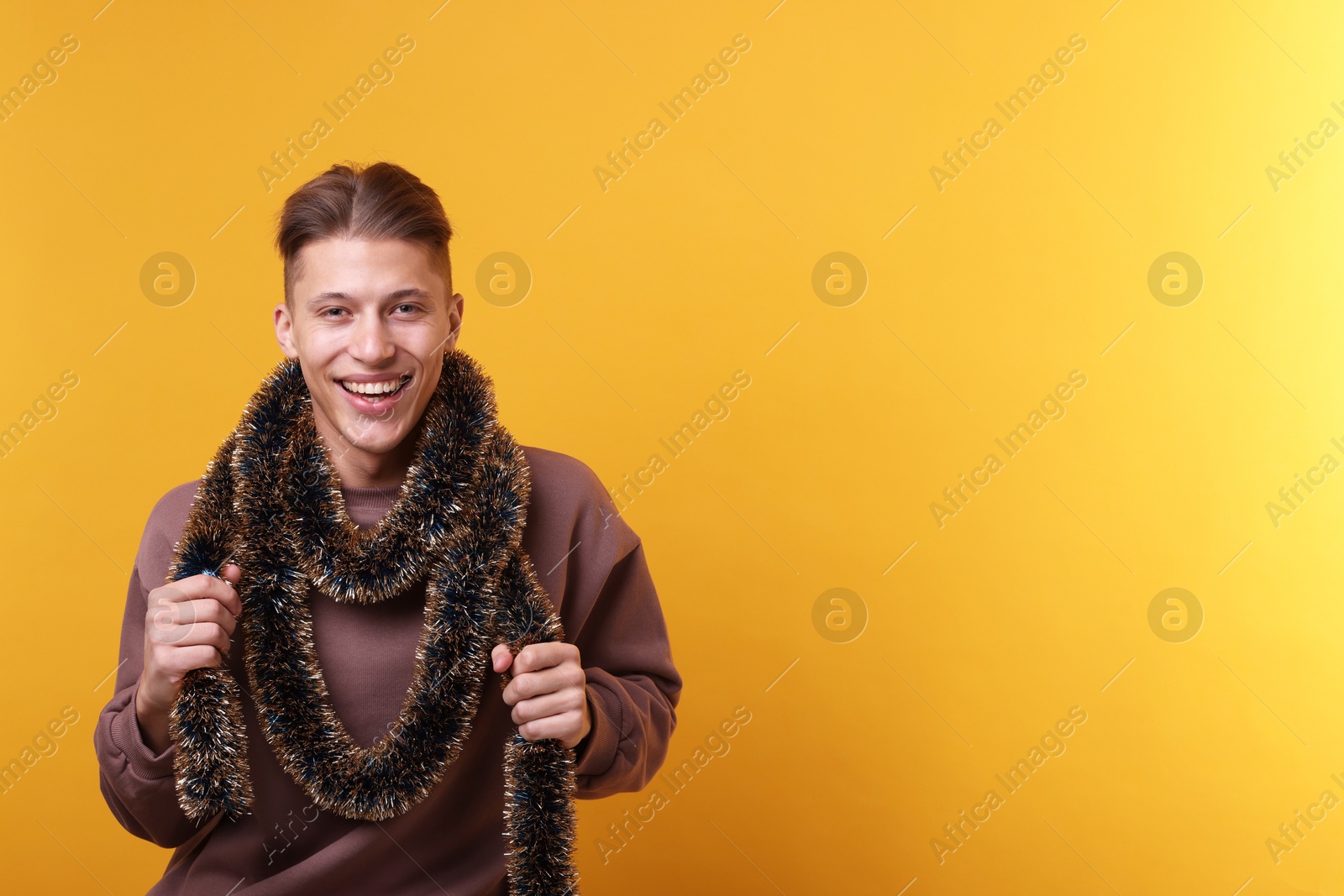 Photo of Happy young man with tinsel on orange background, space for text