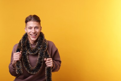 Photo of Happy young man with tinsel on orange background, space for text